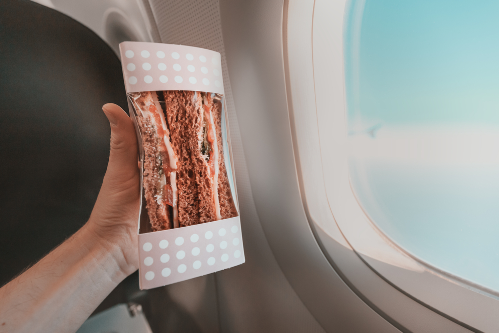 Travel snacks: Sandwiches in hand in the cabin during the airplane flight. Concept of food in the economy segment