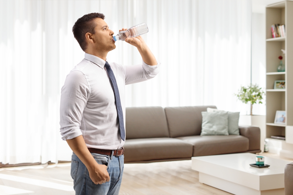 Hydration and Water Filters: picture of a man drinking water from a plastic bottle at home in a living room 