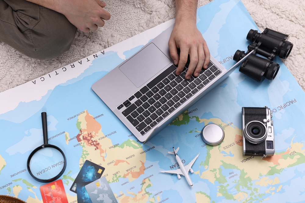 The Best Times to Book Your Travel to Maximize Savings: Travel blogger using laptop and map for planning trip, top view