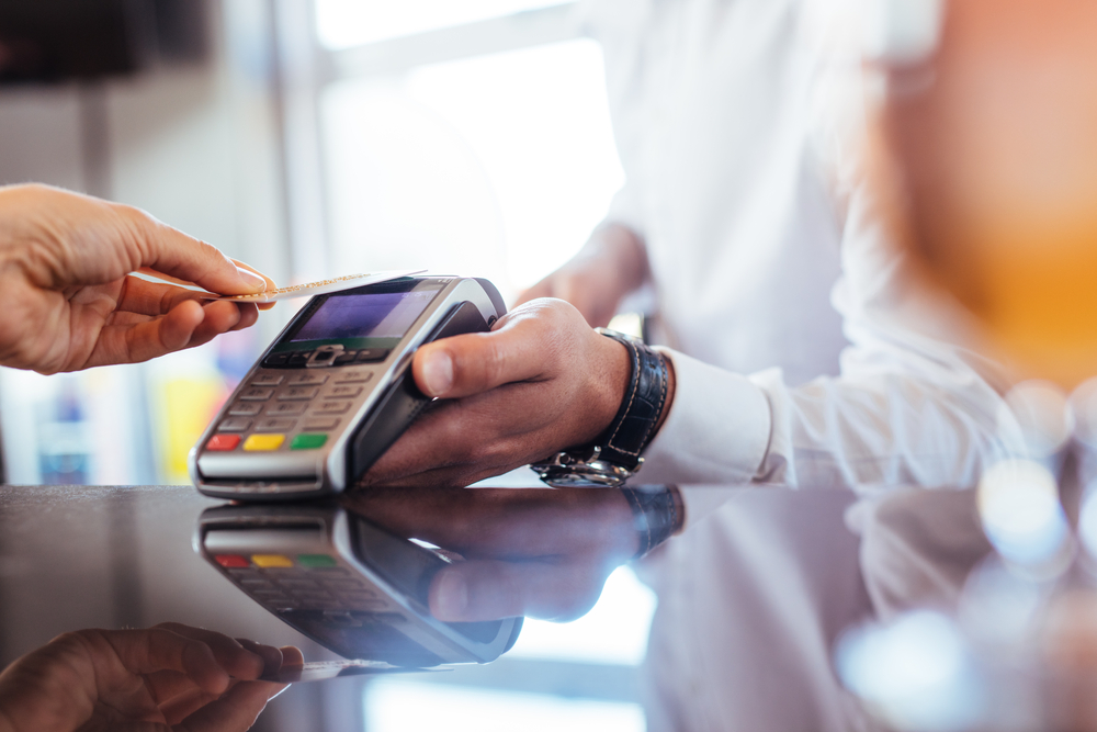 Choosing the Right Credit Card: Hand of customer paying with contactless credit card with NFC technology. Bartender with a credit card reader machine at bar counter with female holding credit card. 