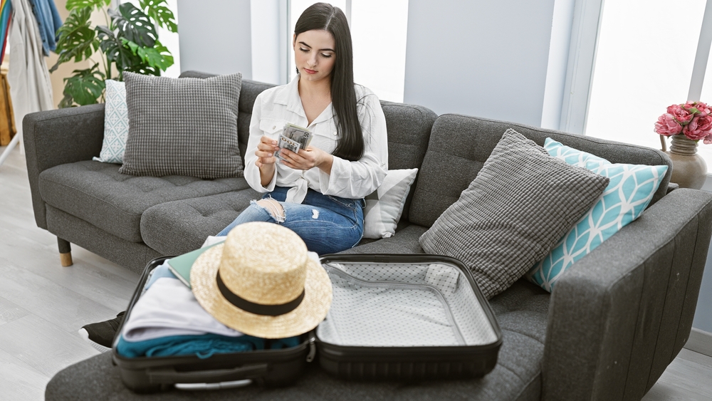 Budget travel: Hispanic Woman Counting Dollars For Vacation Sitting On Couch 