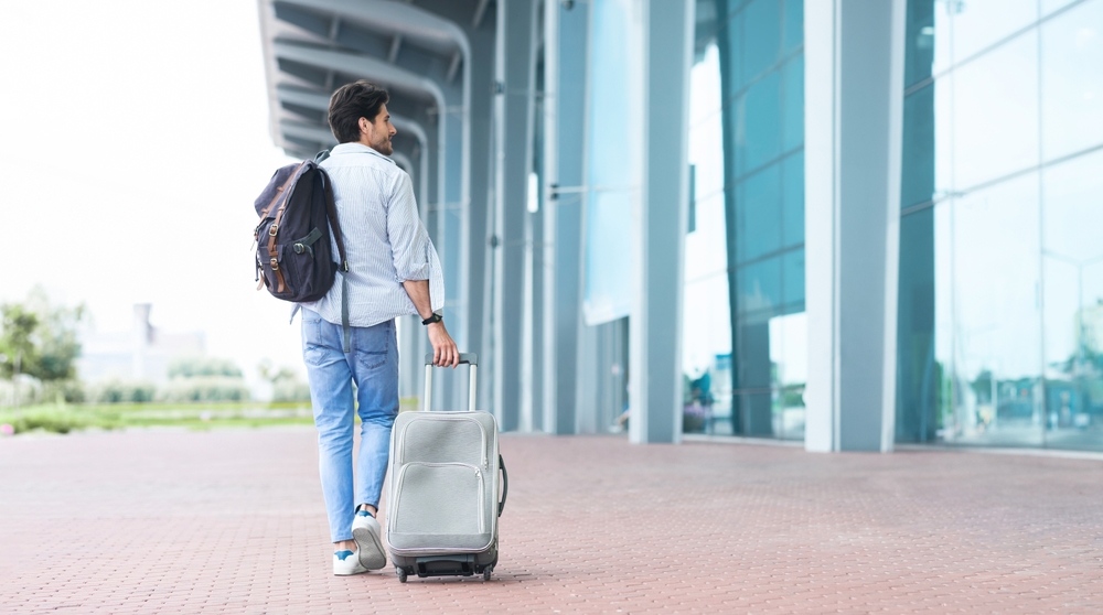 The Art of Traveling Light: Essential Tips for Minimalist Packing: Man Traveller Arrived To Airport, Walking With Suitcase And Backpack Outdoors, Looking For Right Terminal To Enter 