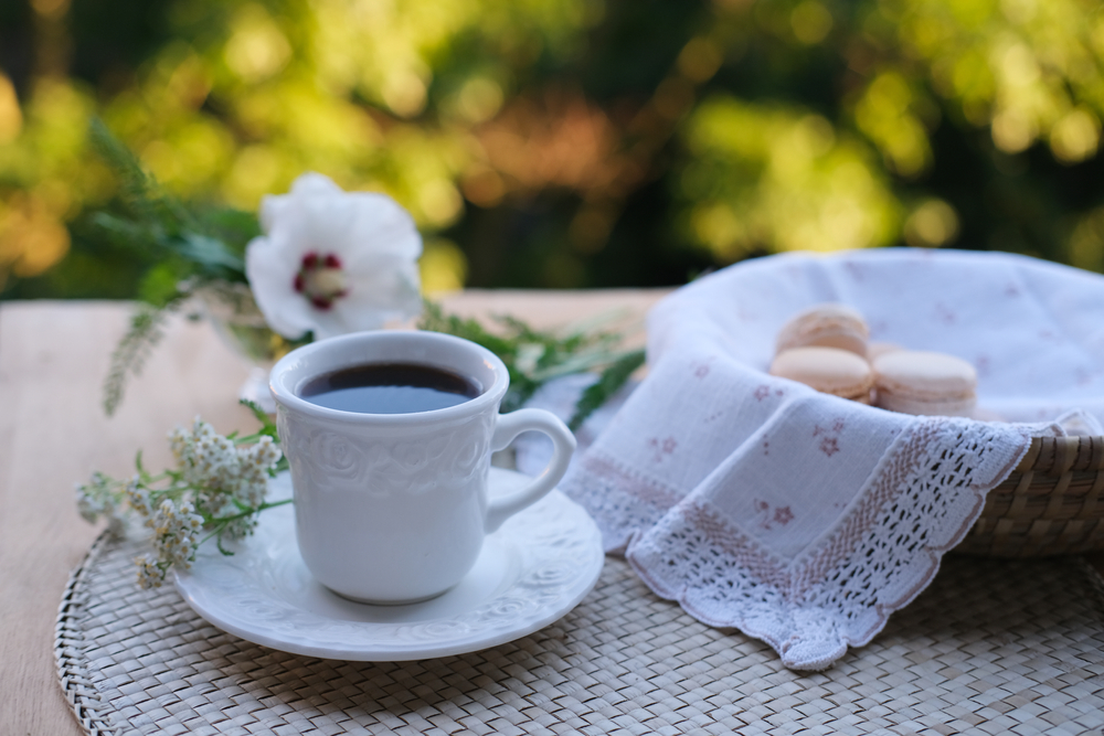 A Guide to Local Artisanal Products in Meteora: tea in a white cup, macaroni cakes in a wicker plate with a napkin, white flowers, concept of summer tea on the terrace, herbal drink with yarrow and hibiscus, breakfast