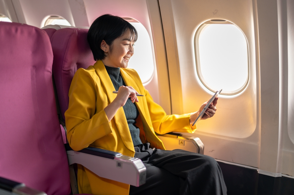 How to Score the Best Deals on Flights Every Time: An over-the-shoulder view of a businesswoman using a laptop on an airplane, capturing the essence of modern travel and work flexibility. 