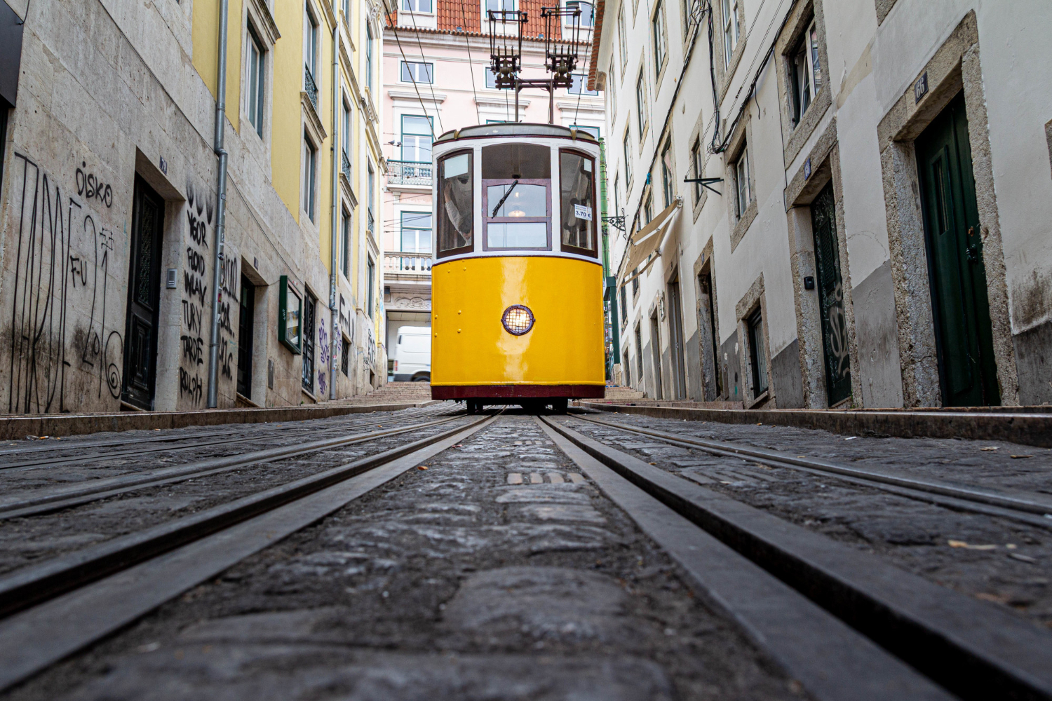 A Visitor's Guide to Getting Around Lisbon’s Trams: Yellow tram going down a narrow alley surrounded by old buildings 