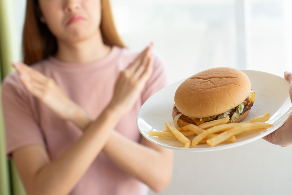 The Worst Foods to Avoid Eating While Traveling Internationally: Woman doing cross arms sign to refuse junk food or fast food (hamburger and potato fried) that have many fat.