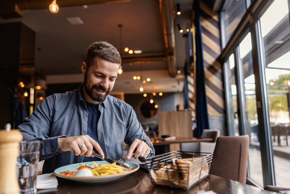 Secrets to Enjoying Luxury Travel on a Budget: A cheerful young man is having breakfast at the restaurant.