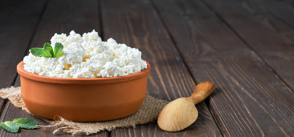 A Guide to Local Artisanal Products in Meteora: Farmer's cottage cheese in a traditional clay bowl, next to a wooden spoon, a dark wooden background. Close-up, selective focus. 