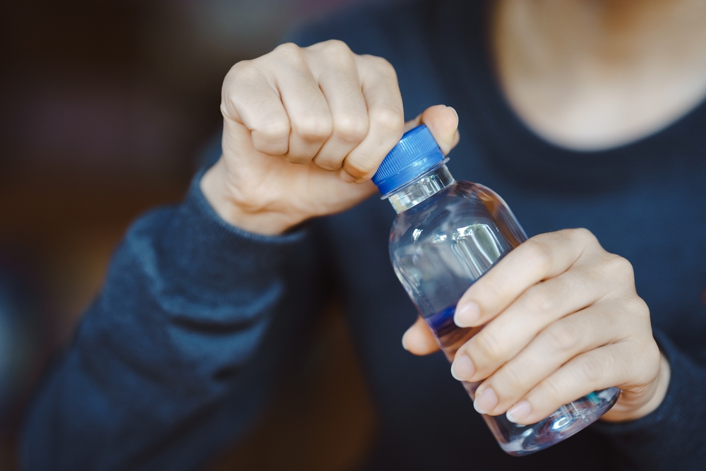 What Not to Do When Drinking Water Abroad: Close-up of hands opening a small plastic water bottle. Concept of hydration, daily water intake, and healthy lifestyle in everyday life. 