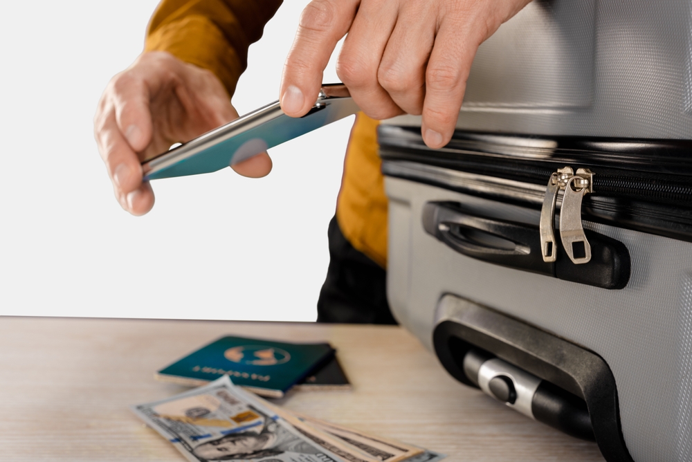 Managing Cash or Cards Money Abroad: Male tourist in airport using smartphone app to count money for trip, on a light gray studio background