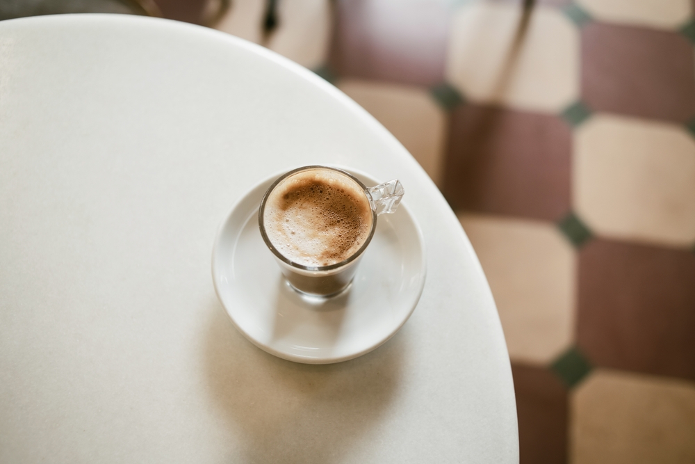 The Role of Coffee in Lisbon's Social and Cultural Fabric: Black coffee in glass cup with coffee beans and jumping drop, on wooden table 