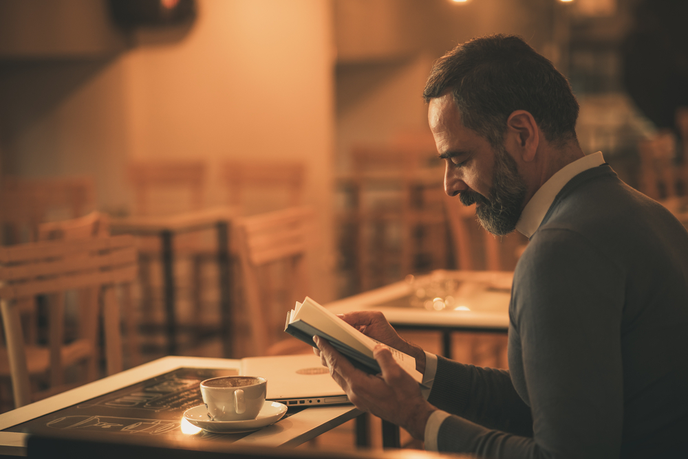 Bookshops and Historic Libraries to Explore: Senior old man reading a book in a coffee shop, enjoying his literary hobby