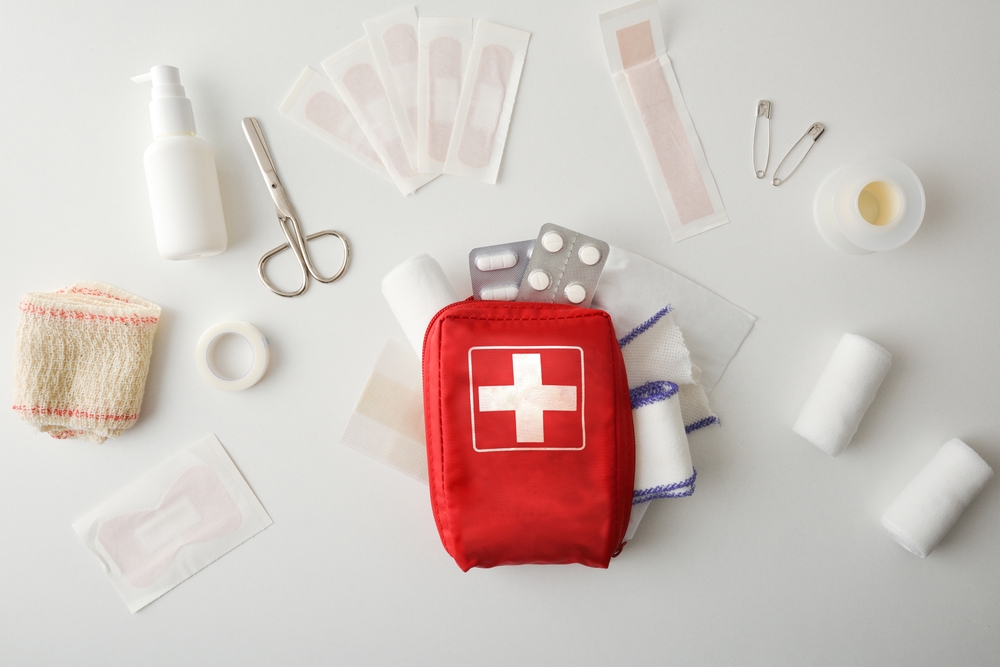 The Worst Mistakes to Avoid When Packing Your Travel First Aid Kit: Travel portable first aid bag full of objects and tools for minor cures on white table. Front view. Horizontal composition 