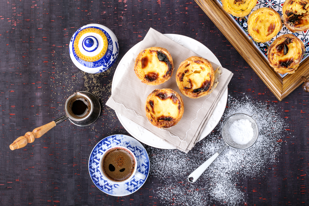 The Role of Coffee in Lisbon's Social and Cultural Fabric: Egg tart, traditional Portuguese dessert, pastel de nata on a parchment paper. Blue textile background 