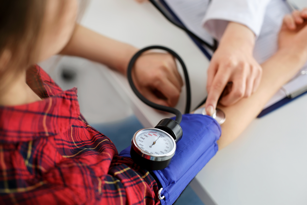 The Biggest Health Risks to Avoid When Traveling to Tropical Destinations: Close up view of a female medicine doctor measuring blood pressure to her patient.