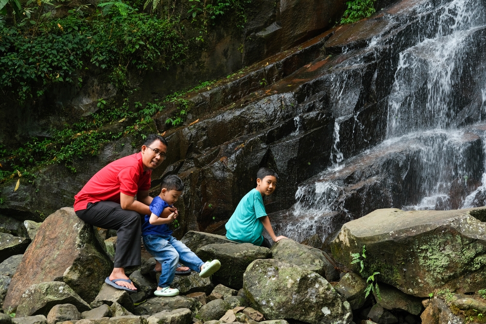 Creative Family Vacation Ideas That Go Beyond the Beach: A family enjoys a scenic view at the base of a majestic waterfall surrounded by lush greenery. Perfect for travel, adventure, nature, family outings, tourism promotions, and environmental conservation 