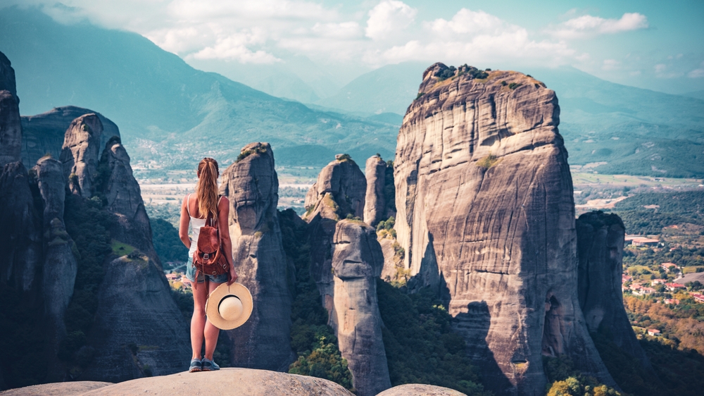 Walking Tours of Meteora: Young woman standing on cliff enjoying Famous Meteor mountain landscape panoramic view in Greece- Meteora