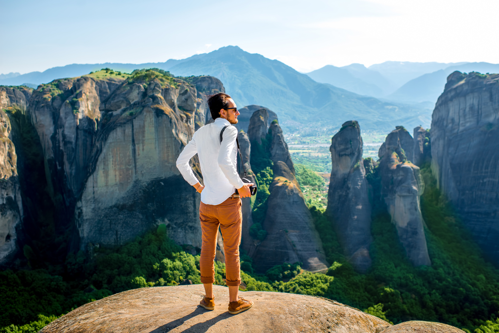 Night Sky Photography in Meteora: Professional well-dressed photographer sitting on the top of mountain on beautiful scenic clif background near Meteora monasteries in Greece 