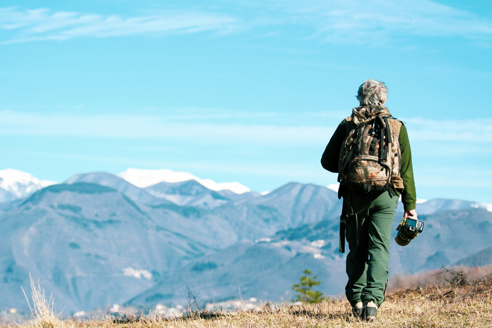 What Not to Do When Hiking: Hiker senior man with backpack and camera walking on the mountain path - Active traveler pensioner - Discovery travel destination concept, Motivation - copy space - main focus on the right 