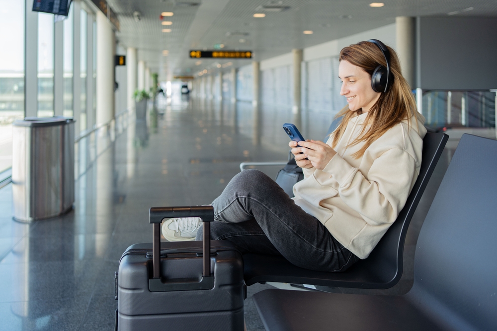 What Not to Do When Choosing Travel: Woman use smartphone and earphones while waiting for her flight, student girl listening to music or podcast at the airport while waiting for a flight