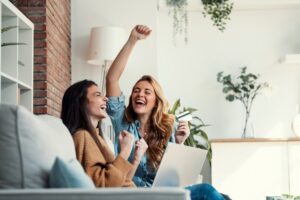 Shot Of Two Happy Young Women Using Computer While Paying